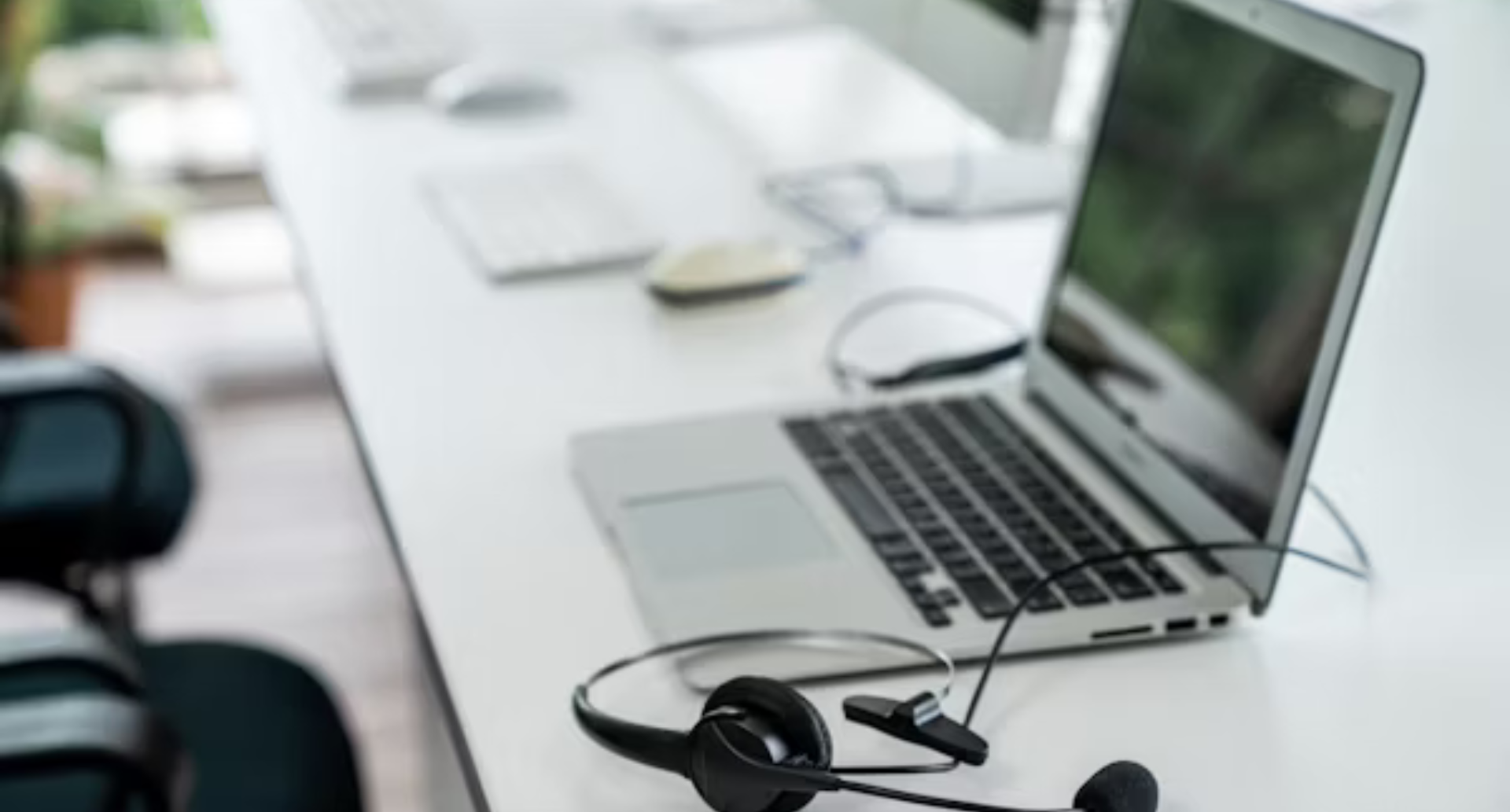 Laptop and VOIP headset on a white office desk in a modern workspace.